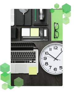 A top-down image of a laptop on a table next to a clock, office supplies and glasses.