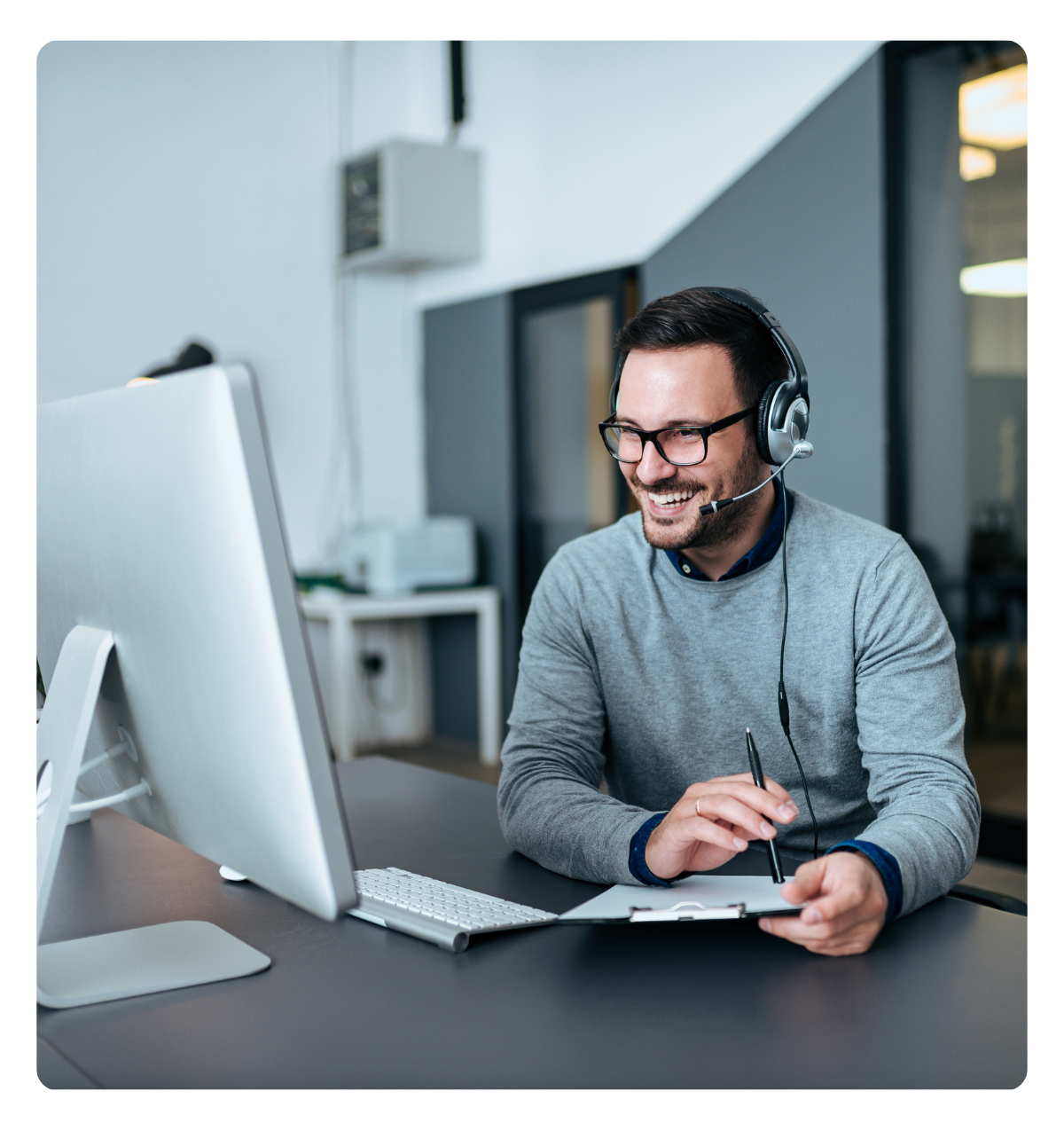 A smiling person working on a computer and talking on a headset.